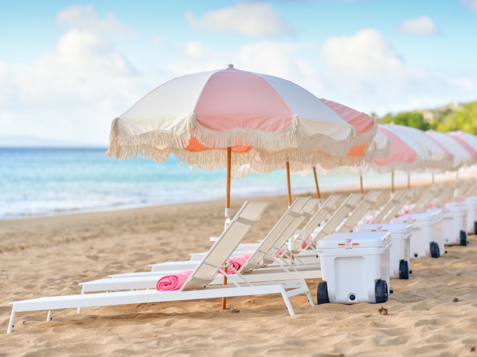 Beach chairs with pink umbrellas and coolers facing the ocean