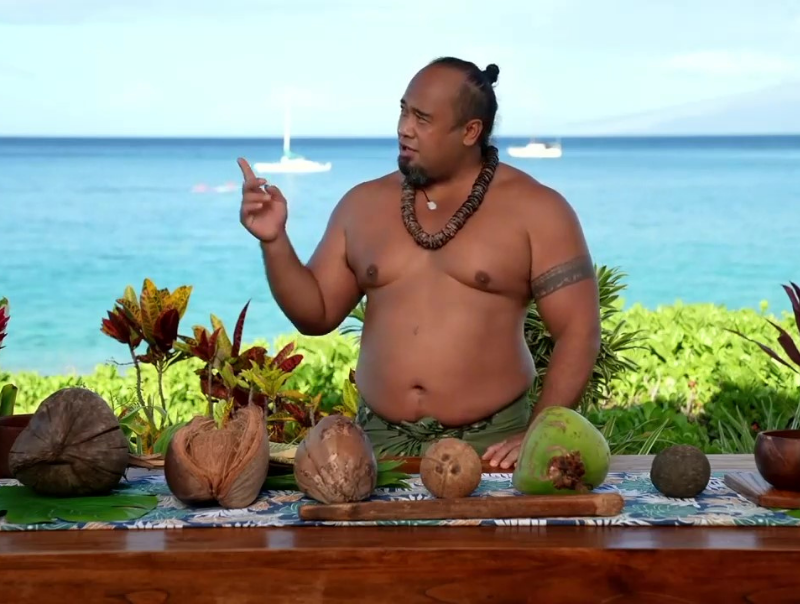 There was a man standing on a table with a row of coconuts