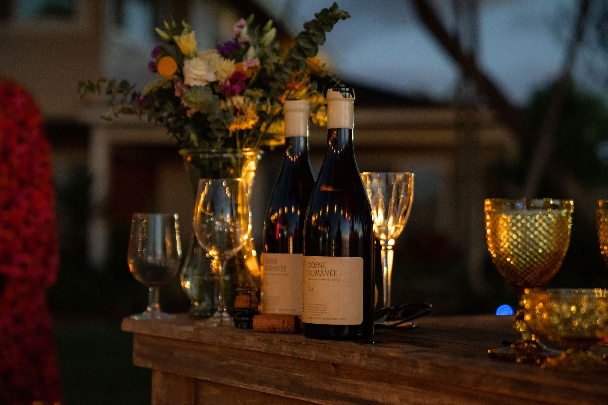 On the wooden table were two bottles of wine, some glasses and bouquets of flowers