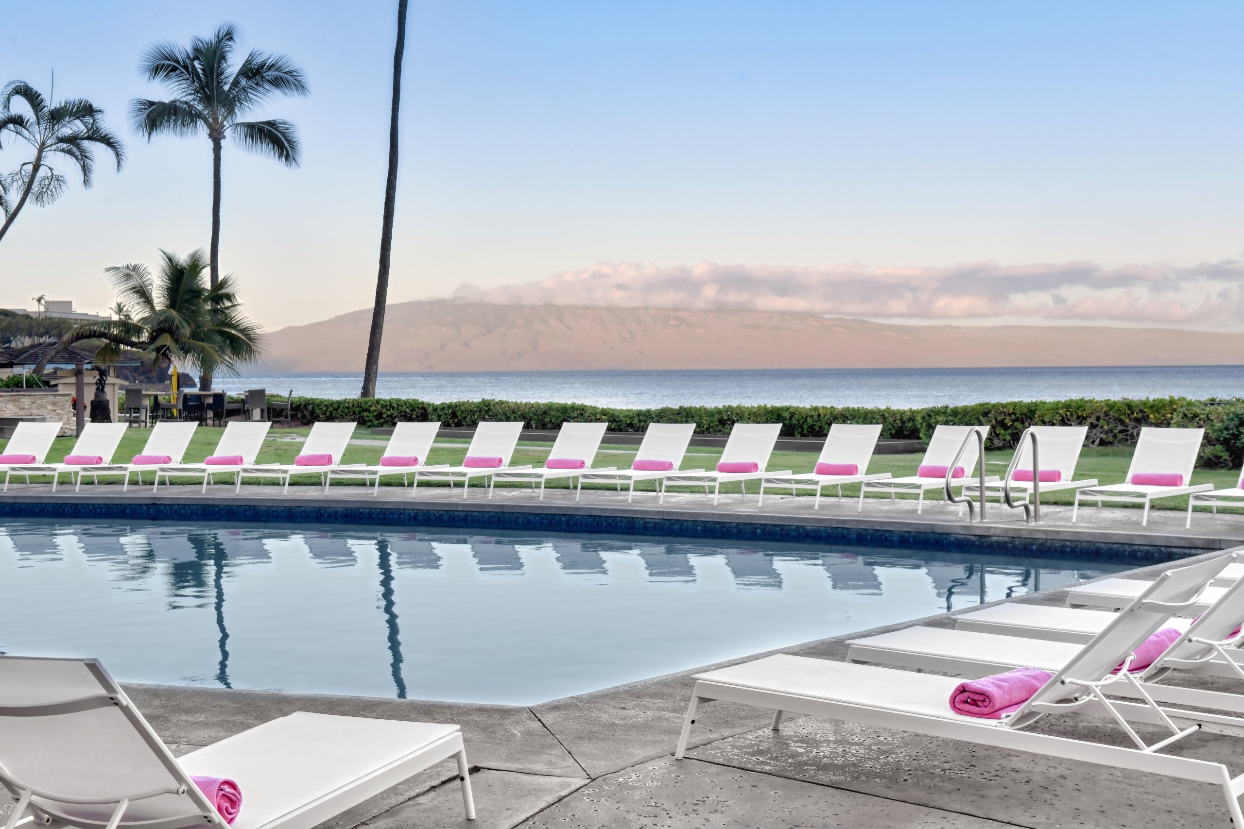Lounge chairs with pink beach towels setup around a pool