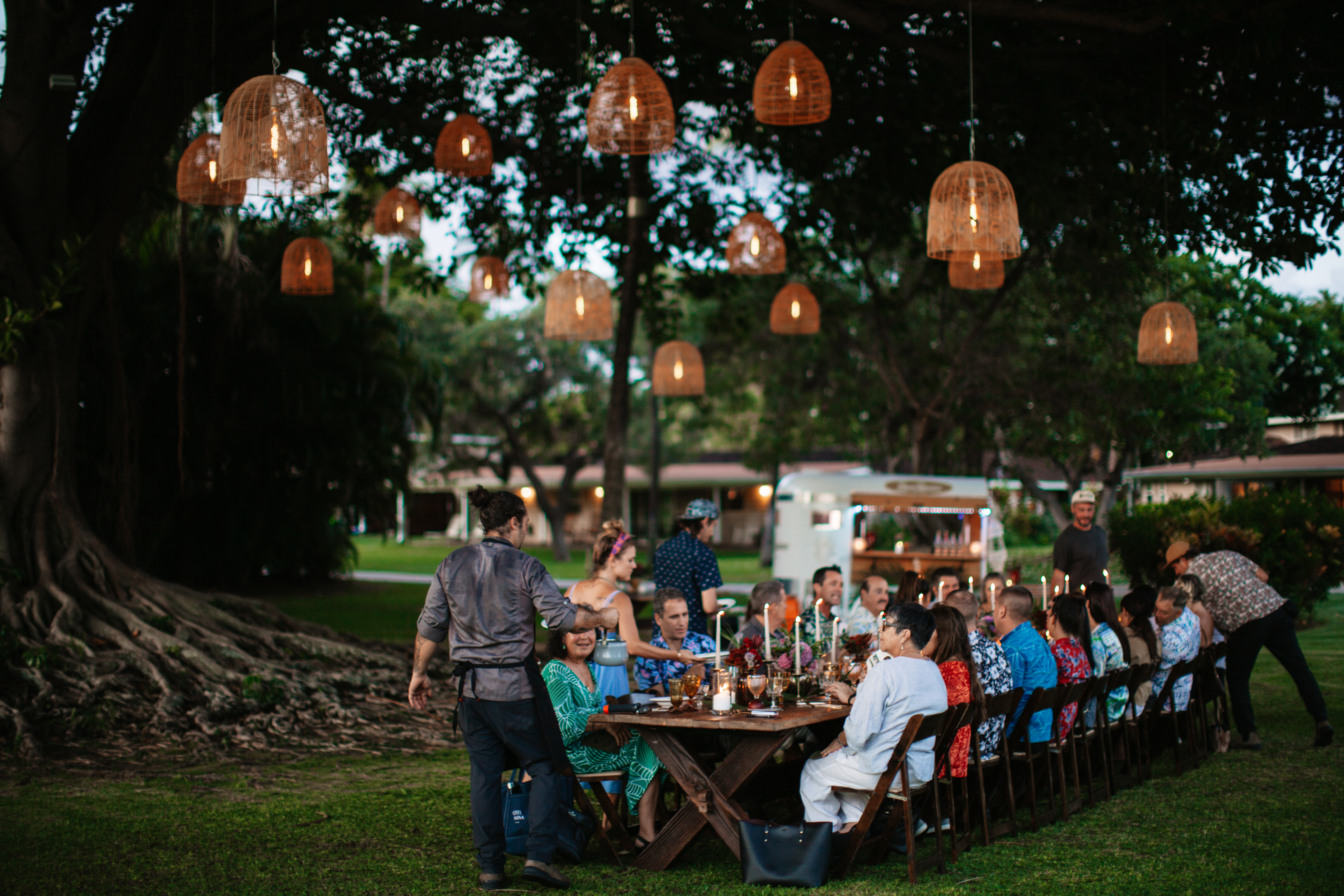 A group of people sitting at a long table outdoors with candlelight and hanging lights