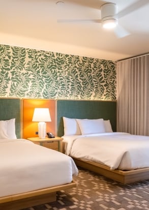 A hotel room with two twin beds, a ceiling fan, and a lamp on a nightstand.