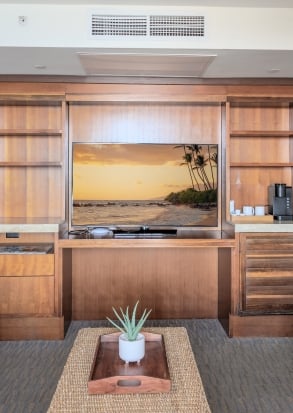 A living room with a large TV showing a beach scene, a coffee maker, and a plant on a wooden tray.