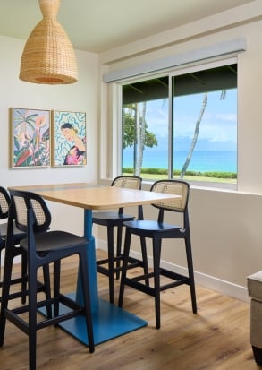 A dining area with a table and bar stools in front of a large window overlooking the ocean.