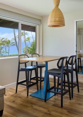 A dining area with a table and chairs, a pendant light, and a window with a view of palm trees.