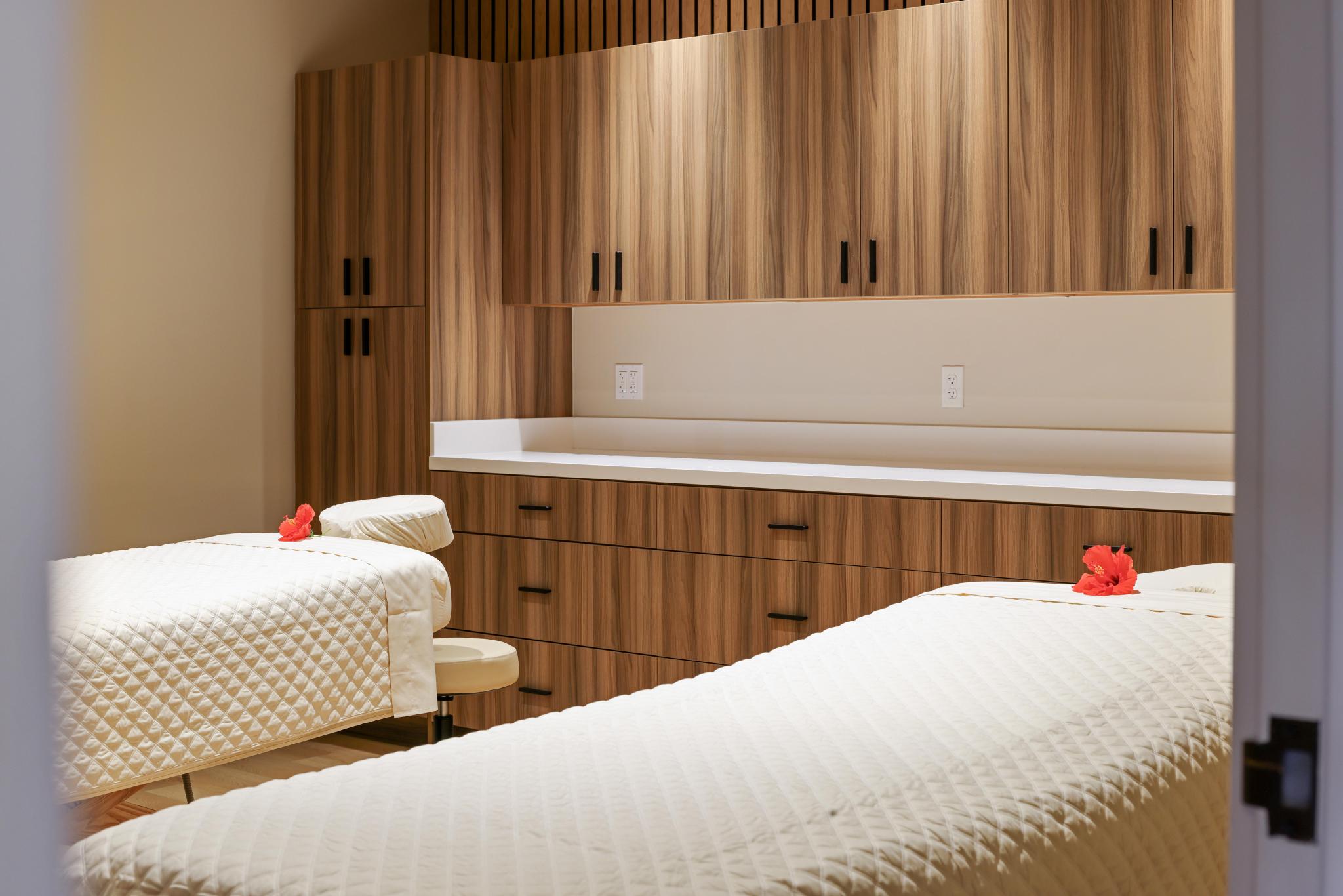 A spa room with two massage tables, wooden cabinets, and white countertops.