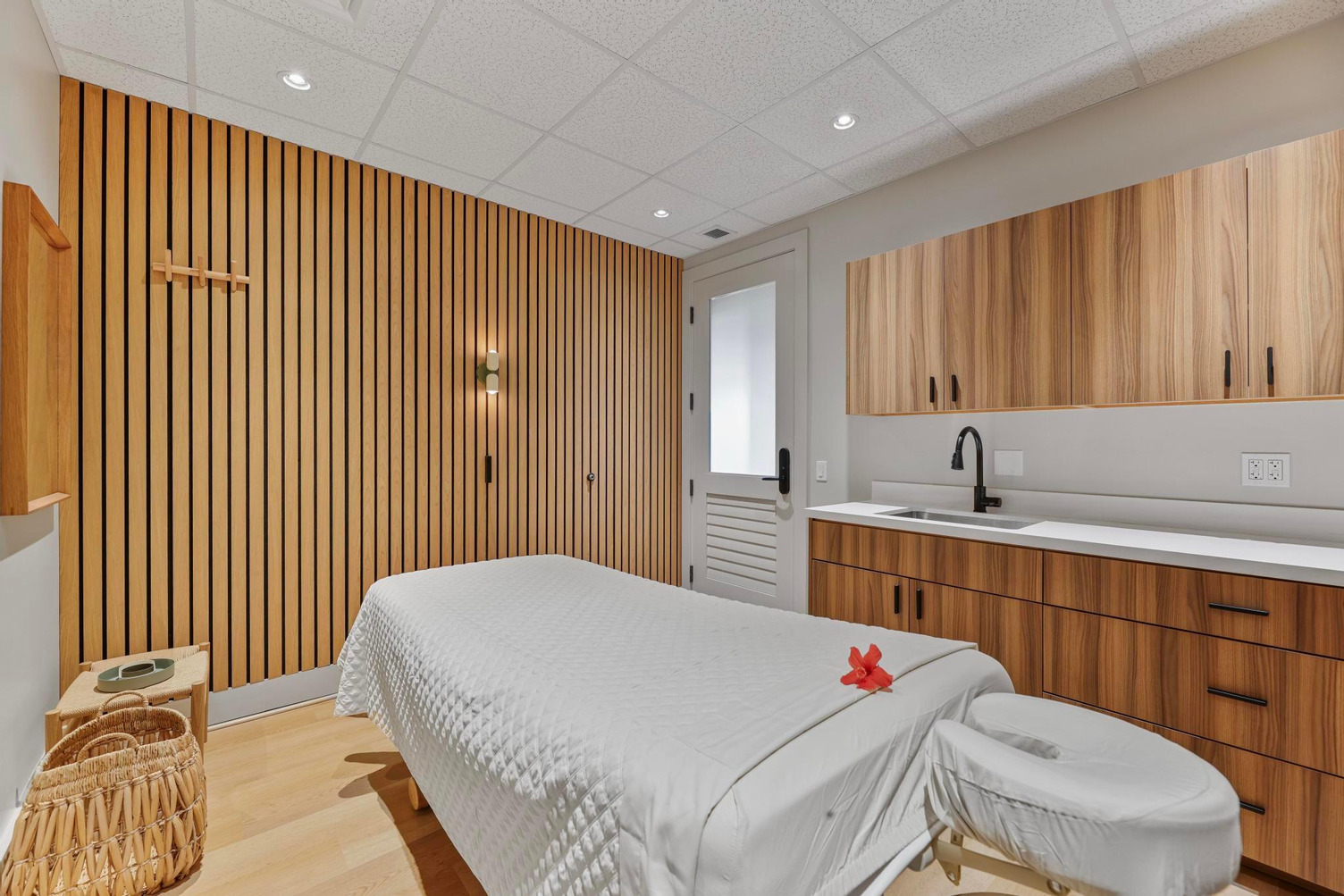 A serene spa room with a massage table, wooden cabinets, and a sink.
