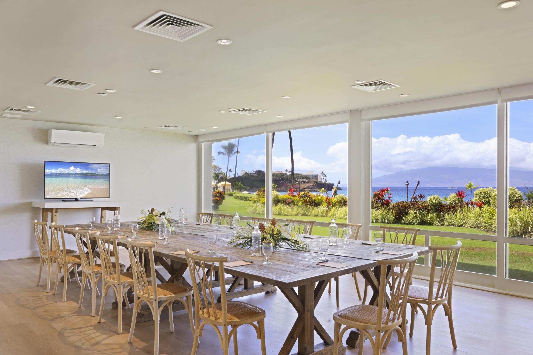 A large meeting room with a long wooden table, glass windows, and a floral centerpiece.